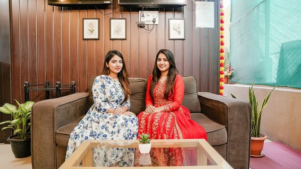 A room with a wooden paneled wall, a flat-screen TV mounted above a sofa, framed artwork on the wall, and potted plants. - Fabhotel Komfort Inn (Pune)