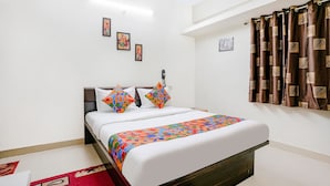 A neatly arranged bedroom with a bed, pillows, a bedside table, a telephone, and a window with curtains. - Fabhotel Komfort Inn (Pune)