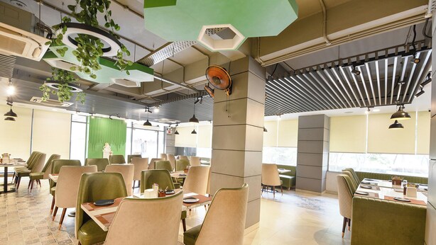 Ein modernes Restaurant mit grünen und beigen Stühlen, sechseckigen Deckenverzierungen und einem großen Ventilator.