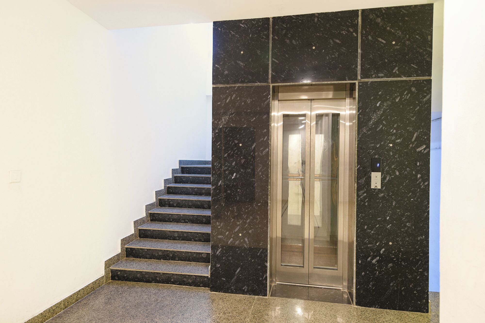 Eine Treppe führt zu einem Aufzug in einem Gebäude mit schwarzen Marmorwänden und einem polierten Granitboden.