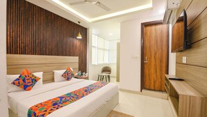 Ein modernes Hotelzimmer mit einem großen Bett, einem hölzernen Kopfteil, einem Deckenventilator, einem Fernseher und einer kleinen Sitzecke.