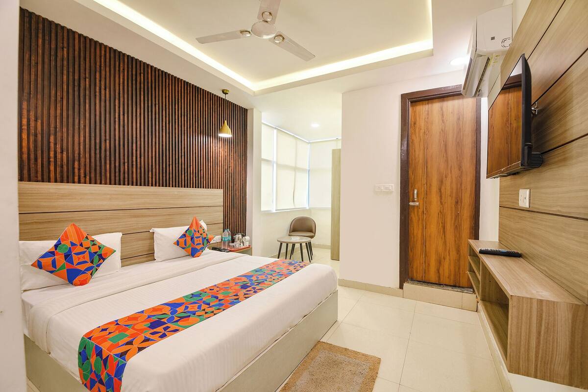 A modern hotel room with a large bed, a wooden headboard, a ceiling fan, a TV, and a small seating area.