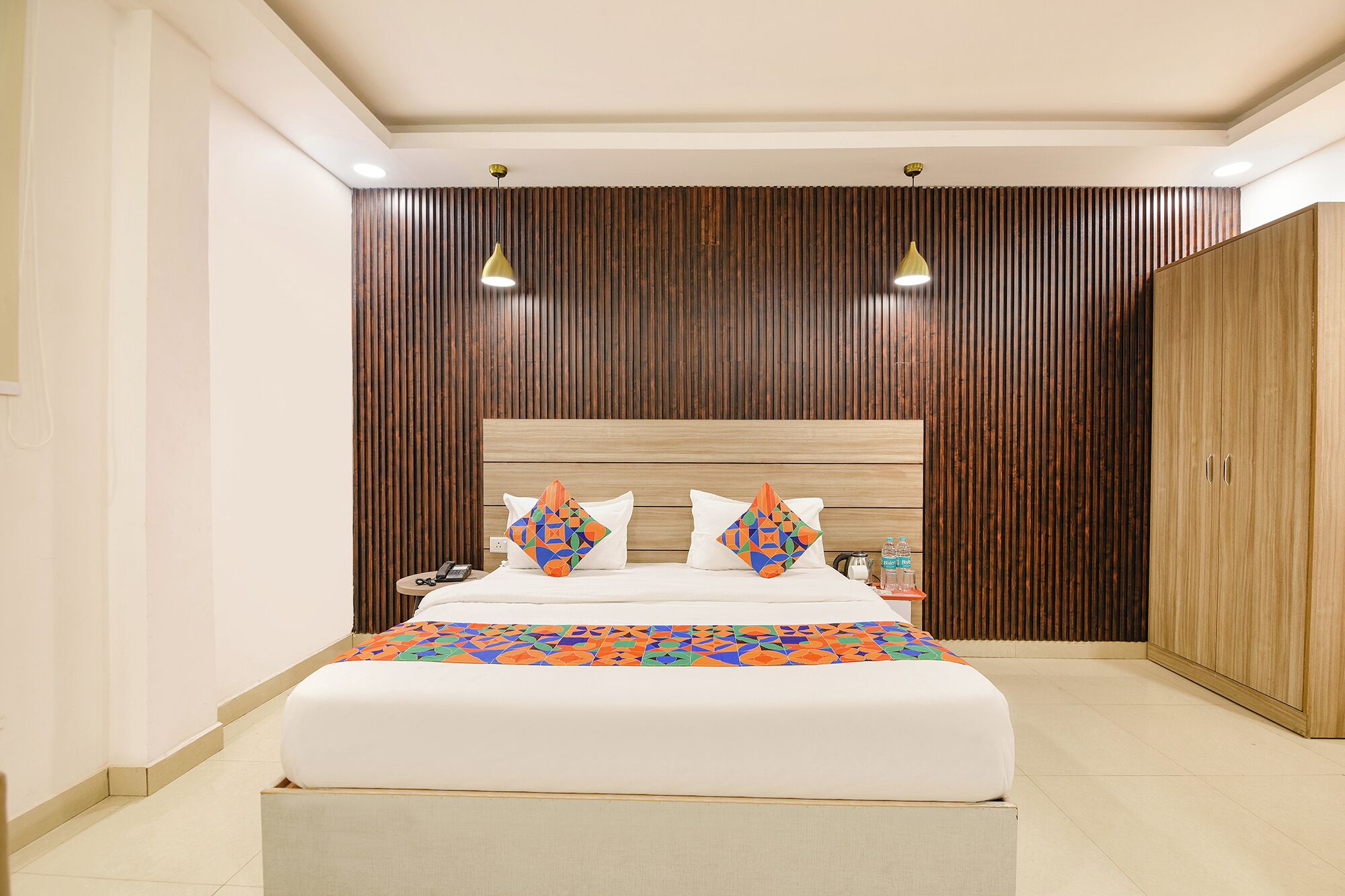 A modern hotel room with a large bed, wooden panel wall, and two pendant lights.