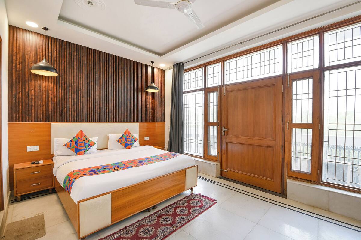 A bedroom with a wooden headboard, a bed with colorful pillows, a nightstand, a large window with a view, and a ceiling fan.
