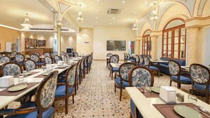 A spacious dining area with long tables and chairs, a restroom sign, and a decorative ceiling. - Oriva Ganeshwaram 149 (Noida)