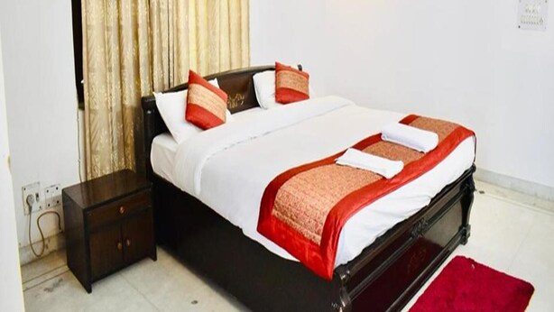 A neatly made bed with white and red linens, a dark wooden headboard, and a red rug on the floor. - Fabhotel Noida Dreamz (Noida)