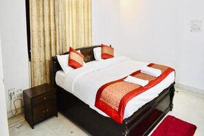 A neatly made bed with white and red linens, a dark wooden headboard, and a red rug on the floor. - Fabhotel Noida Dreamz (Noida)