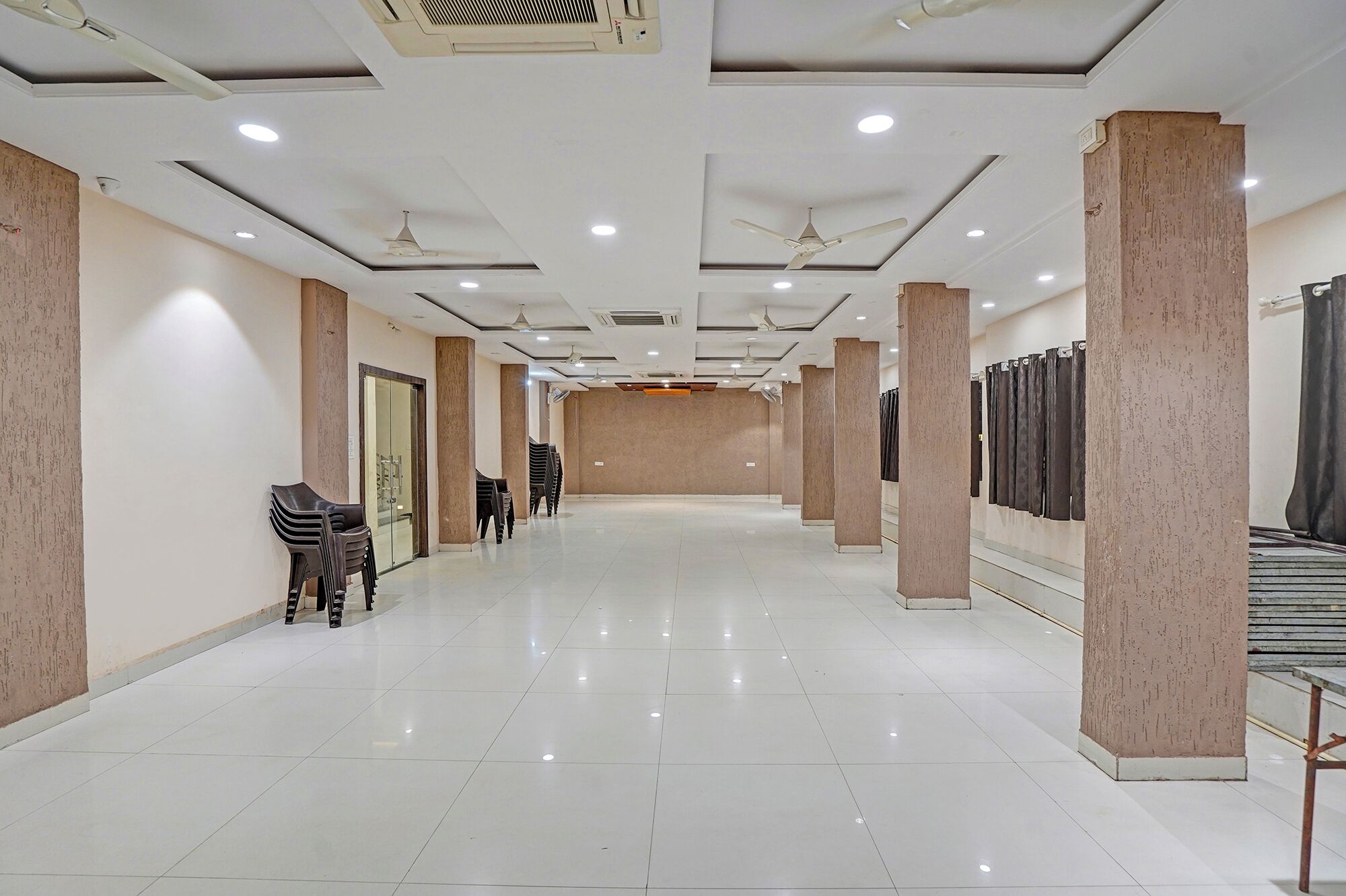A spacious hallway with white tiled floors, beige walls, and multiple ceiling fans.