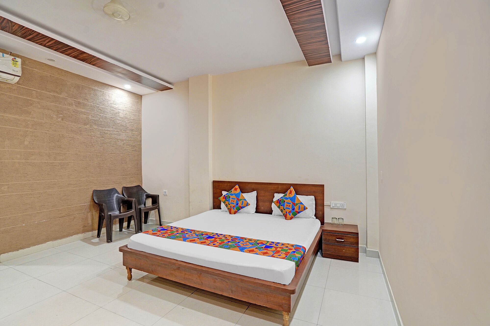 A bedroom with a wooden bed, two pillows, a nightstand, and two chairs.