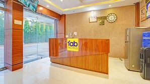 A hotel reception area with a wooden reception desk, a clock, and a refrigerator. - Fabhotel Paras Palace (Bhopal)
