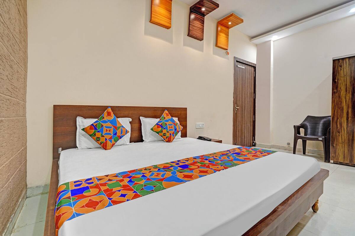 Uma cama bem arrumada com um edredom e almofadas estampadas com um padrão geométrico colorido, uma cabeceira de madeira e uma porta de madeira ao fundo.