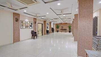 A spacious lobby with a high ceiling, recessed lighting, and a central seating area with chairs and a table.