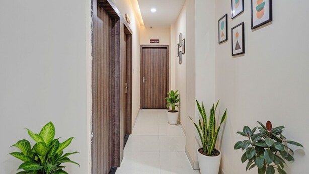 A hallway with a wooden door, potted plants, and framed artwork on the walls. - Fabhotel Paras Palace (Bhopal)