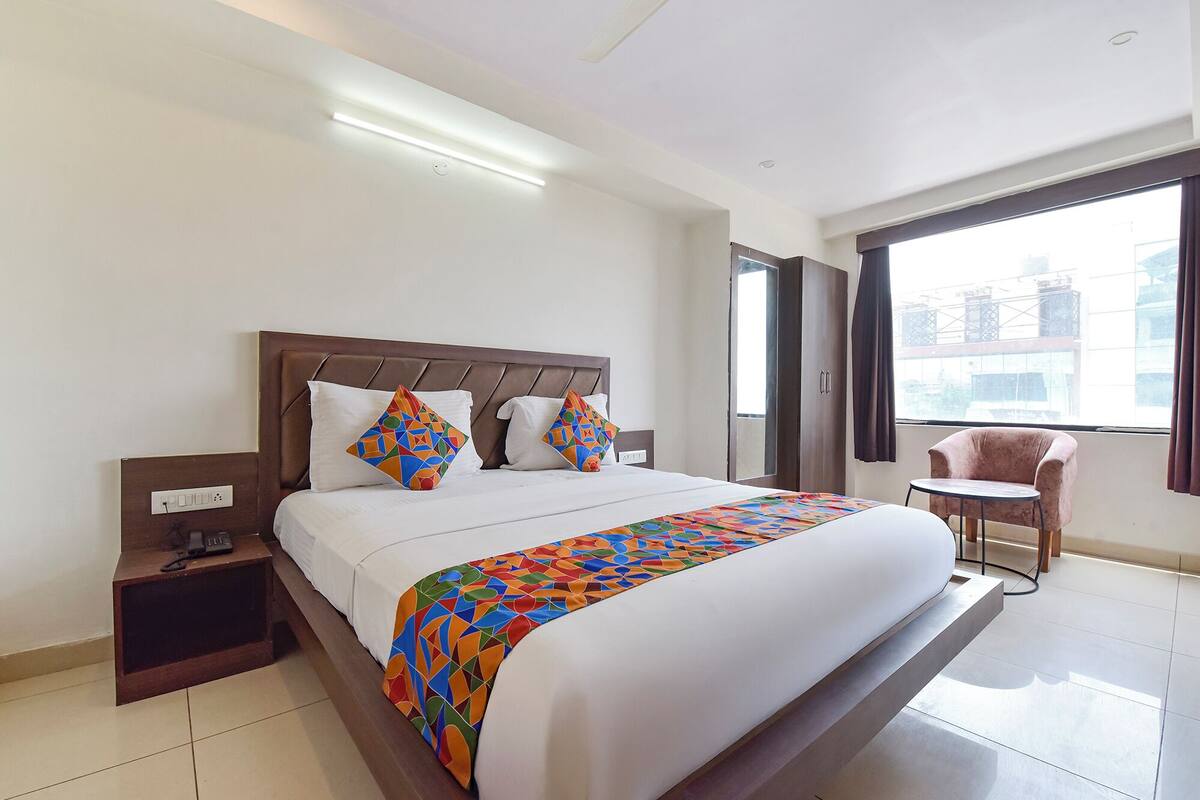 Une chambre d’hôtel avec un grand lit, une table de chevet avec un téléphone, une chaise près de la fenêtre et une vue sur les bâtiments environnants.