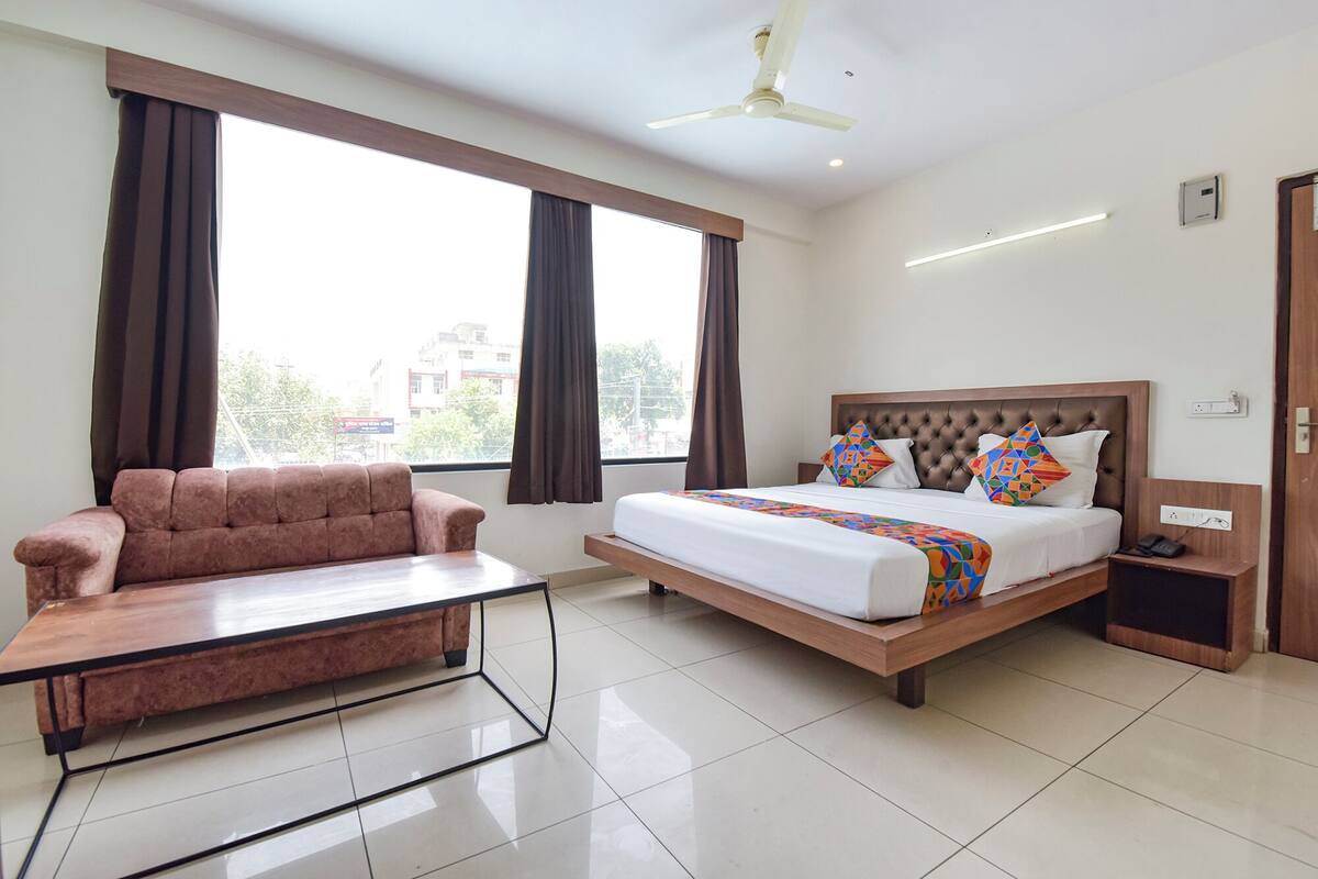 Une chambre d’hôtel comprenant un lit, un canapé, une table de chevet, une commode et un ventilateur de plafond.