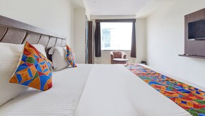 A hotel room with a bed, a chair, a TV, and a window with a view of buildings. - Fabhotel The Grand Manmuralidhar (Jaipur)