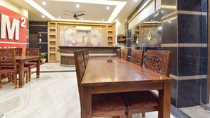 A spacious dining area with a long wooden table and chairs, a ceiling fan, and a decorative wall mural. - Fabhotel The Grand Manmuralidhar (Jaipur)