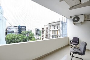 A balcony with a view of a cityscape, a chair, and an air conditioning unit. - Fabhotel Harnoor House (Gurugram)