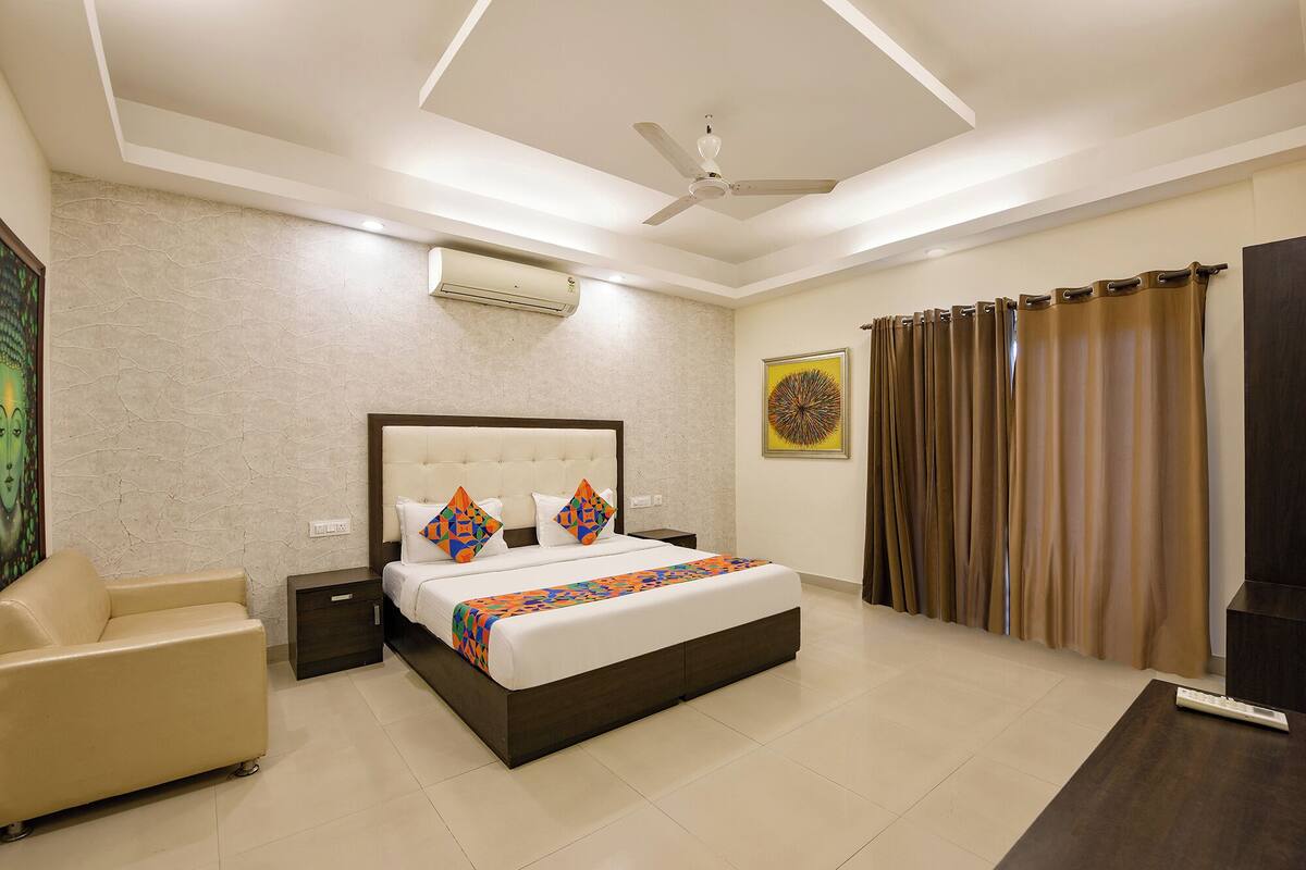 Quarto de hotel moderno com uma cama grande, ventoinha no teto, aparelho de ar condicionado, sofá bege e televisão.