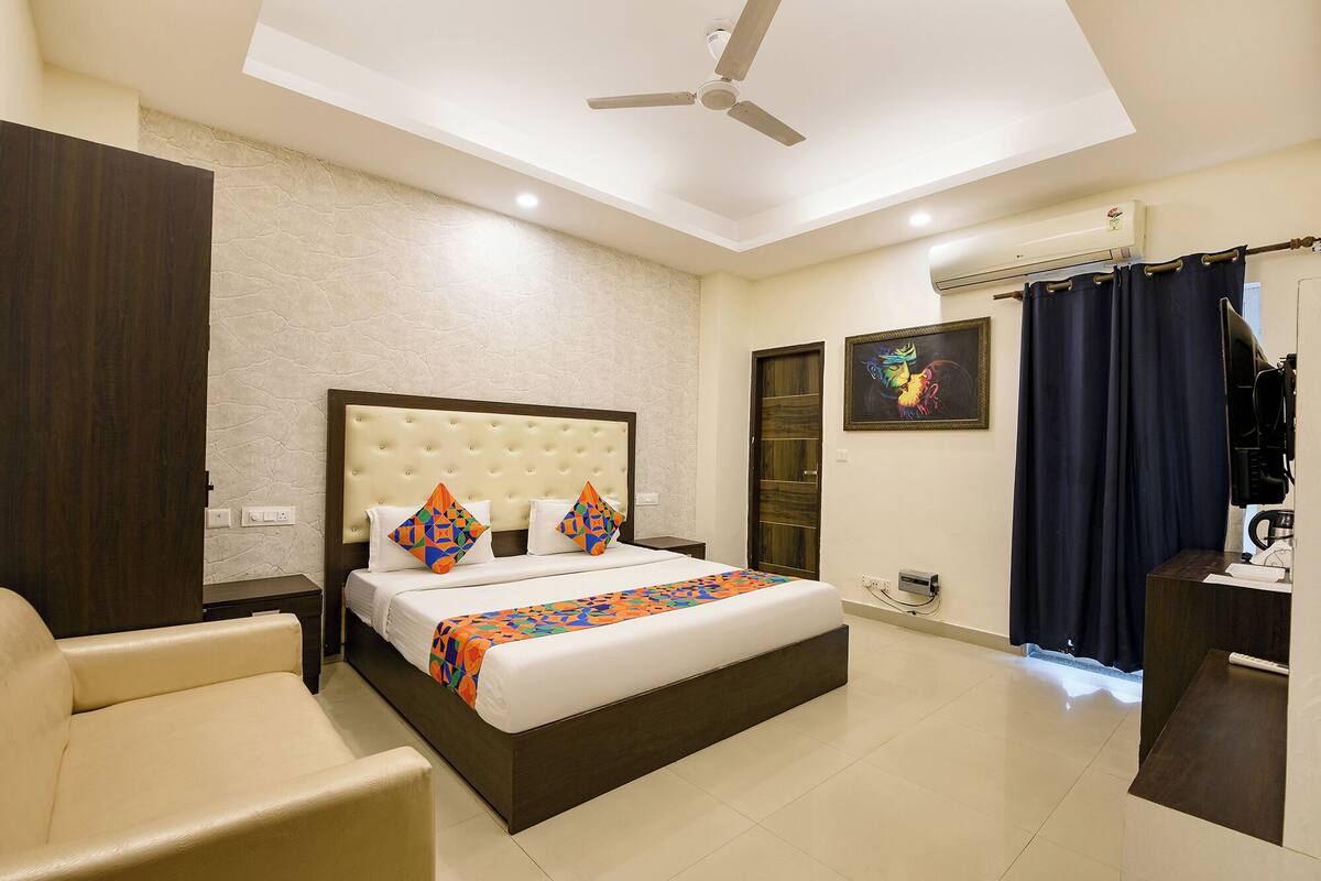 Quarto de hotel com cama, poltrona, ventoinha no teto e ar condicionado, além de uma porta.