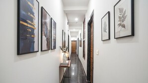 A hallway with framed artwork on the walls, a small table with a vase and books, and a polished black floor. - Fabhotel Devi Heritage (Vrindavan)