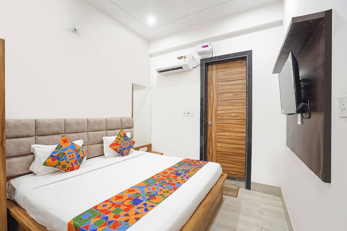 A bedroom with a bed, pillows, a wooden door, and an air conditioning unit.