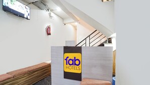 A hotel reception area with a modern design, including a reception desk with a logo, a staircase, and a fire extinguisher on the wall. - Fabhotel Devi Heritage (Vrindavan)