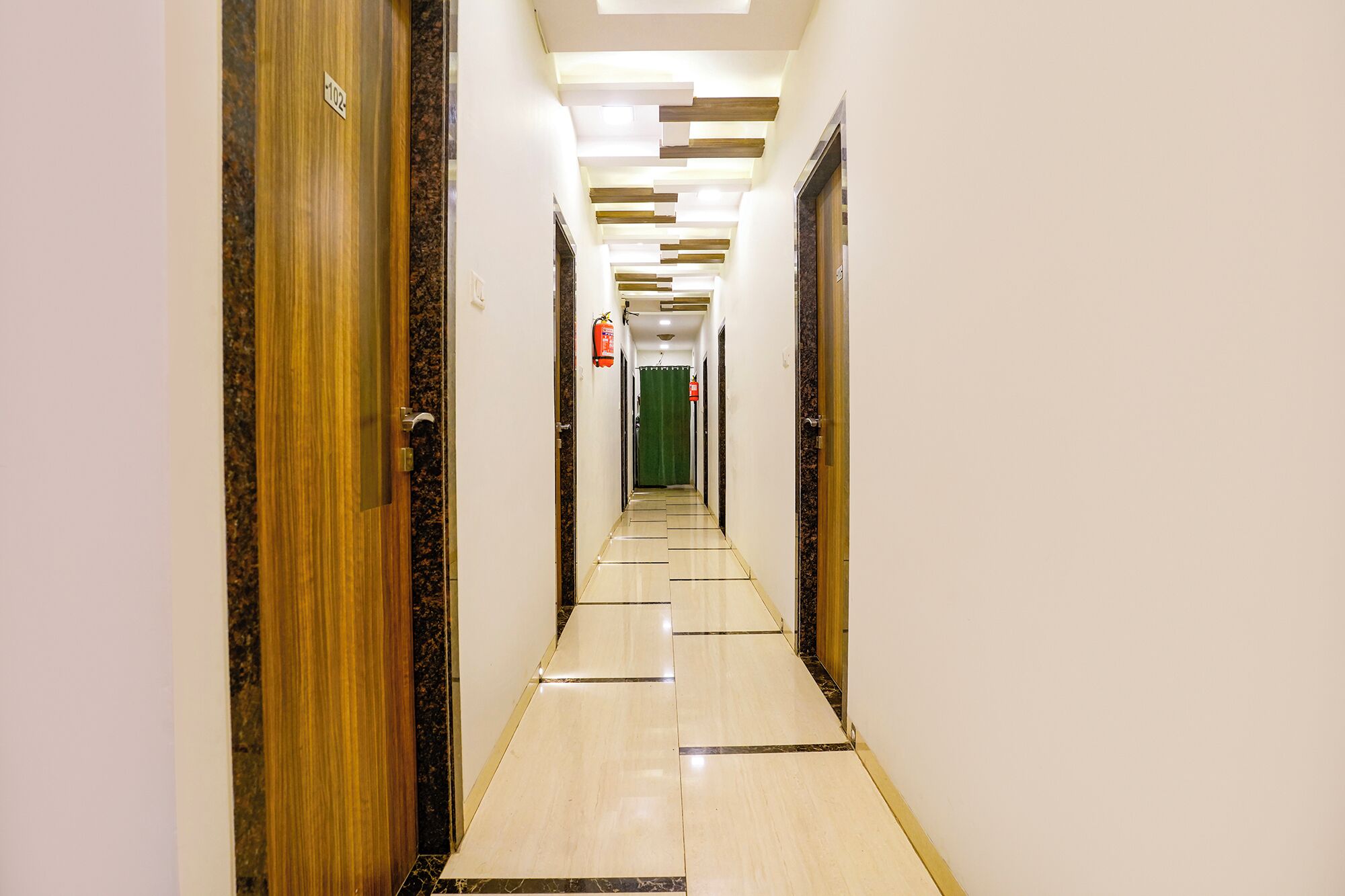 A hotel corridor with wooden doors, a tiled floor, and a green curtain at the end.