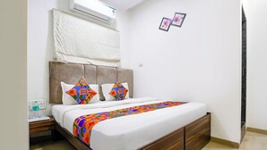 A bedroom with a bed, a nightstand, a water bottle, and a power outlet. - Fabhotel Amfahh Inn (Mumbai)