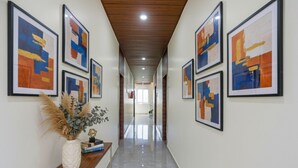A hallway with framed abstract art on the walls, a wooden console table with a vase and books, and a polished floor. - Fabhotel Rr Residency I (Khammam)