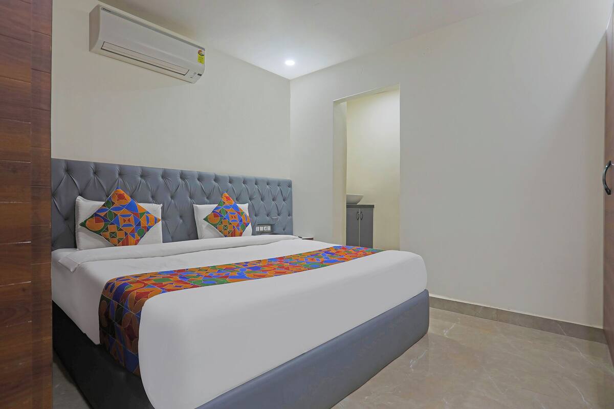 A hotel room with a large bed, a tufted headboard, a modern air conditioning unit, and a small cabinet.