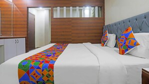 A neatly made bed with a colorful geometric-patterned bedspread, a grey upholstered headboard, and two pillows with a multicolored geometric design. - Fabhotel Rr Residency I (Khammam)