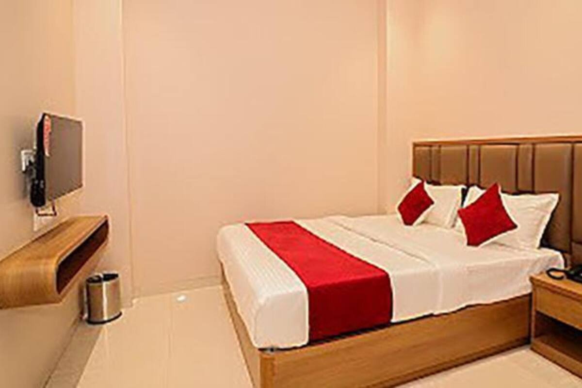 A hotel room with a bed, a bedside table, a TV mounted on the wall, and a trash bin.