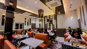 A modern restaurant with orange booths and rectangular tables, featuring a patterned carpet and recessed lighting. - FabExpress Ascent Star Inn (Mumbai)