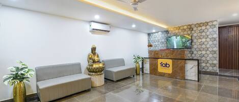 A hotel reception area with a reception desk, a Buddha statue, a sofa, and a ceiling fan.