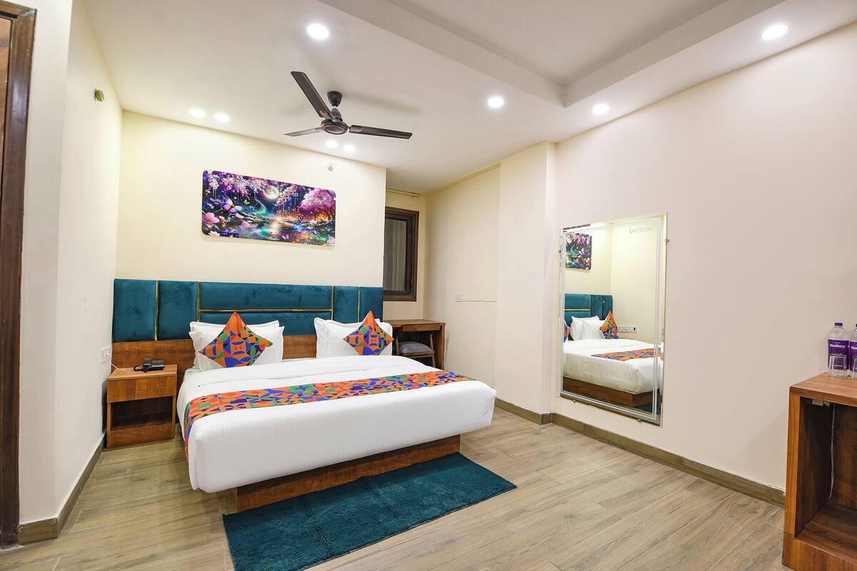 Une chambre d’hôtel avec un grand lit, un ventilateur de plafond, une table de chevet, une commode, un miroir et un plancher en bois.