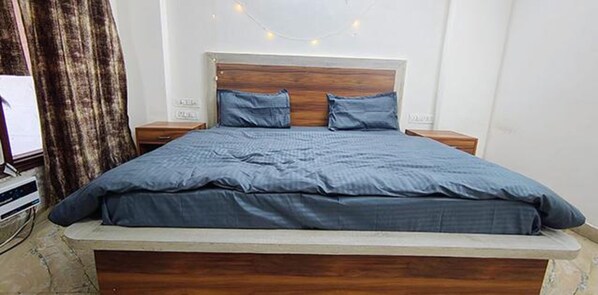 A bedroom with a wooden headboard, two bedside tables, and a bed with a blue bedspread. - Fabhotel Vibe Living (Gurugram)