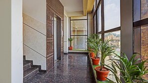 A corridor with a marble floor, potted plants, and large windows offering a view of the city. - FabHotel Galaxy Suites - Near MP Layout Metro Station, Hebbal (Bengaluru)