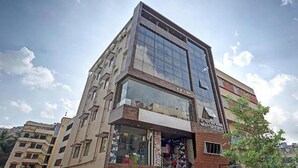 A modern building with a glass facade and a storefront at the ground level. - FabHotel Galaxy Suites - Near MP Layout Metro Station, Hebbal (Bengaluru)
