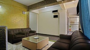 A modern living room with a brown leather sofa, a glass coffee table, and a patterned wall. - FabHotel Galaxy Suites - Near MP Layout Metro Station, Hebbal (Bengaluru)