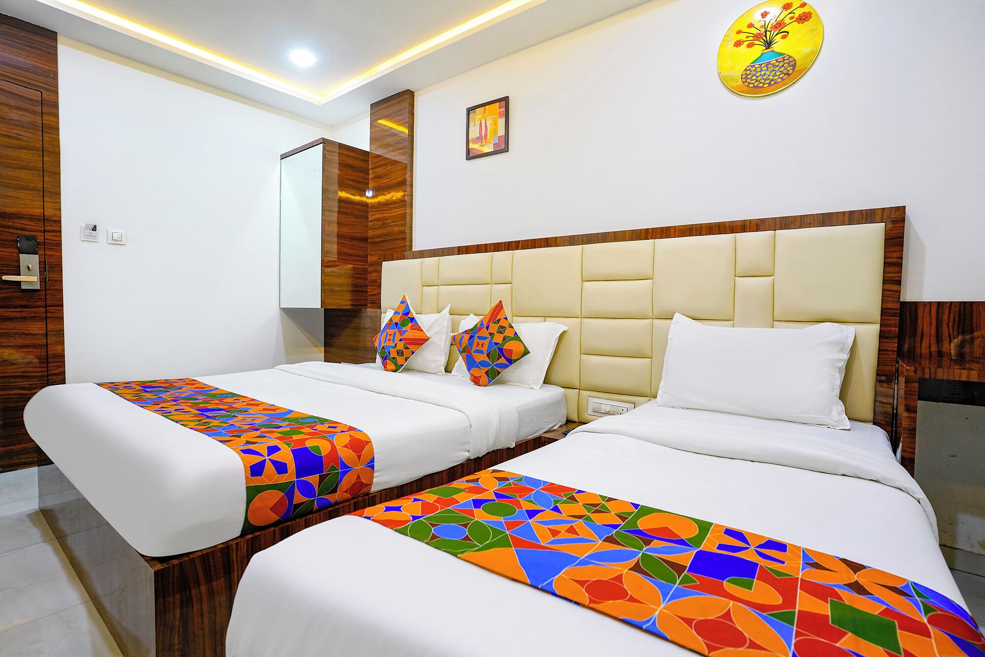 A hotel room with two beds, a wooden headboard, a mirror, and a colorful artwork on the wall.