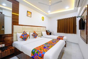 A hotel room with two beds, a wooden headboard, a ceiling fan, a wall-mounted TV, and a bathroom with a shower curtain. - FabHotel Shahi Palace (Mumbai)