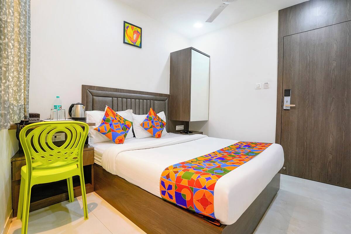 Une chambre d’hôtel avec un lit, une chaise, une table de chevet, un miroir et une porte.