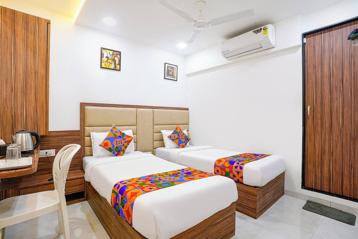 Une chambre d’hôtel avec deux lits, un bureau avec une bouilloire, une chaise et un appareil de climatisation.
