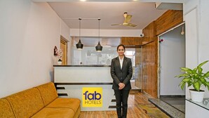 A hotel reception area with a receptionist, a reception desk, a sofa, and a potted plant. - Fabhotel Casa Inn (Barasat)