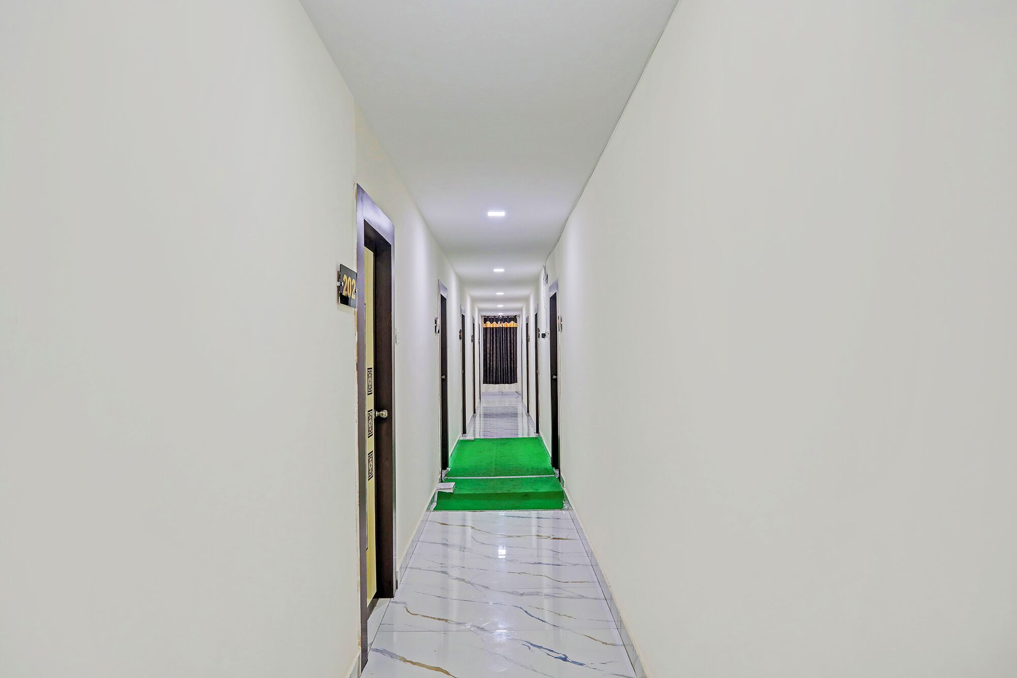 A narrow, well-lit hallway with a green carpet leading to a door marked with the number 202.