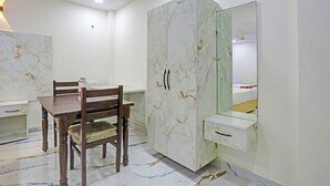 Una habitación con un armario de diseño marmolado, una mesa de comedor de madera con sillas, y una pequeña mesita de noche blanca con espejo.