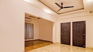 A hallway with marble flooring, a ceiling fan, and two dark wooden doors. - Fabhotel 85 The Seven Wonders (Barasat)