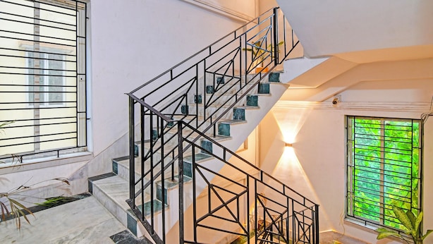 A staircase with black metal railings, marble steps, and a view of greenery outside. - Fabhotel 85 The Seven Wonders (Barasat)