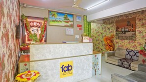 Zona de recepción de un hotel con un mostrador de mármol, un ventilador de techo y un papel tapiz con motivos florales.
